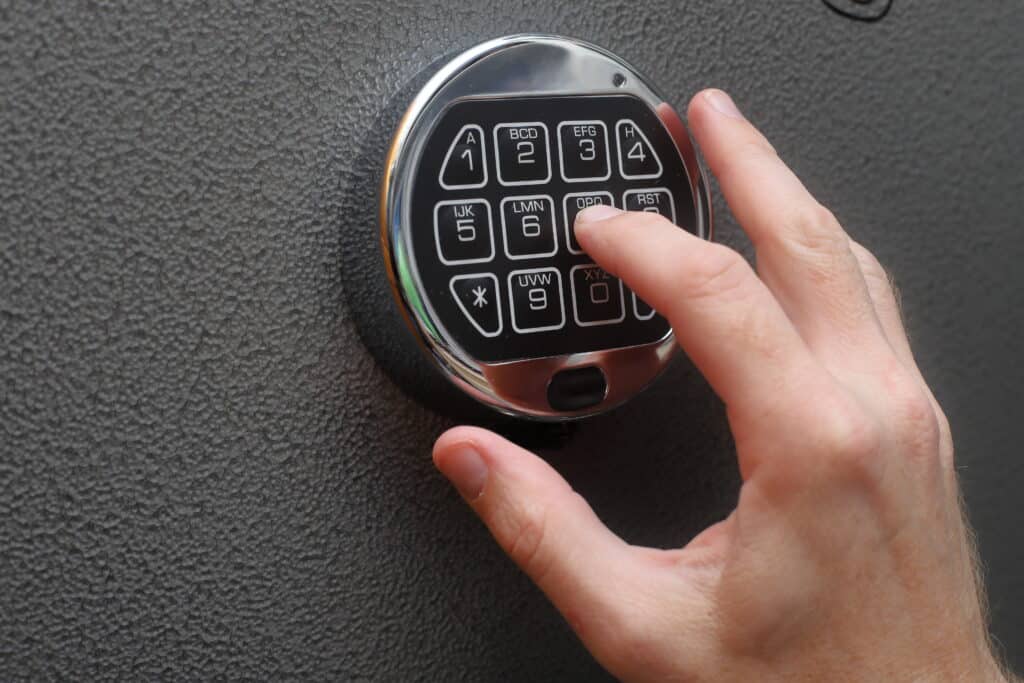 Close-up of fingers pressing a circular metallic electronic keypad on a textured dark surface, as a user enters a code from 1–9 keys.