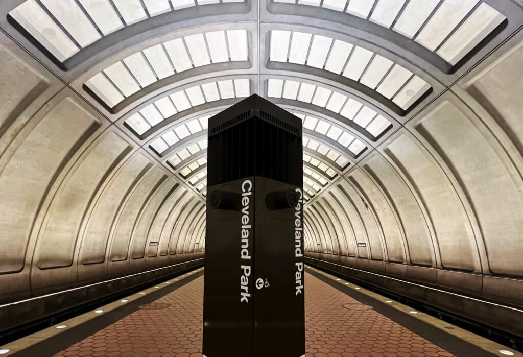 Underground metro platform with arched, tiled walls and a tall black pillar in the center displaying 'Cleveland Park'.