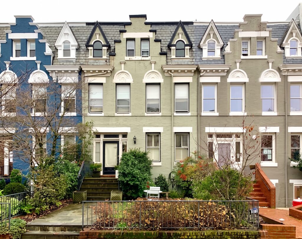 Row of colorful Victorian townhouse facades with arched windows and decorative trim, front steps, and small gardens.