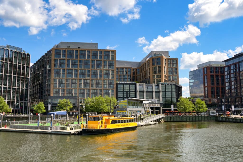Urban waterfront with brick and glass apartment buildings along a river under a blue sky with clouds.