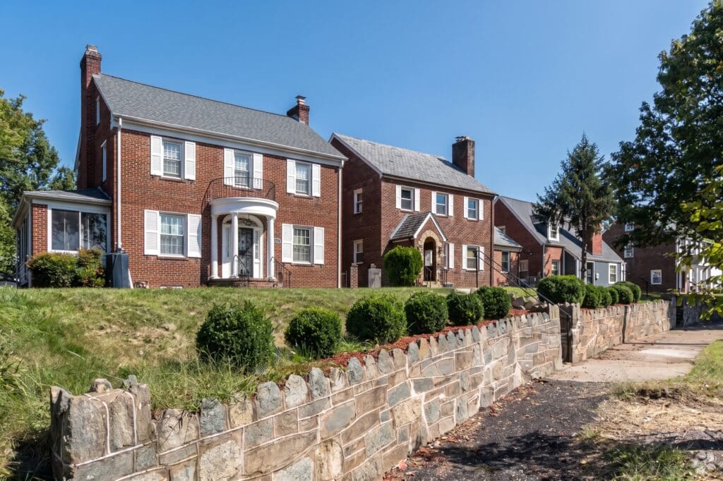 Brick colonial houses on a hillside lot behind a stone retaining wall